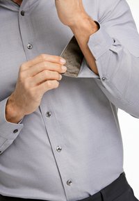 Hellgraues, strukturiertes Button-up-Hemd mit einem kontrastierenden, gemusterten Innenrand. Verfügt über silberne Knöpfe und ein klassisches Kragen-Design.