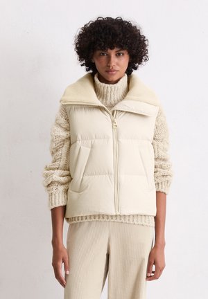 Gilet imbottito crema con colletto alto e chiusura frontale, caratterizzato da ampie tasche laterali e un maglione a maglia crema testurizzato sotto.