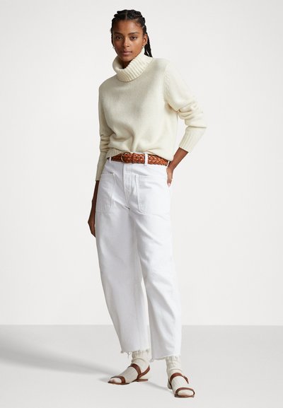 Cream turtleneck sweater, white relaxed-fit pants, braided brown belt, and brown sandals with cream socks. Minimalist design, textured fabric.