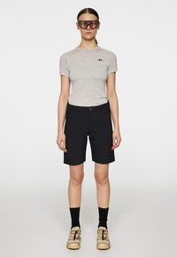 Harmaa lyhythihainen paita, mustat shortsit ja beigeet kengät. Kevyt materiaali, ihonmyötäinen muotoilu ja huomaamaton brändäys paidassa ja shortseissa.