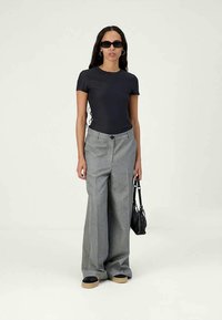 Black fitted t-shirt paired with light grey wide-leg trousers. Accessorized with black sunglasses and a small black handbag.
