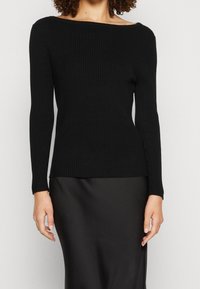 Pull noir à manches longues avec côtes, col bateau large ; coupe ajustée, tissu texturé et finition lisse à l'ourlet, assorti à une jupe noire.