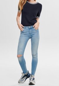 Námořnická košile s krátkým rukávem a bílými detaily, světle modré roztrhané skinny džíny a šedé tenisky s námořnickými akcenty. Ležérní střih a denimová textura.