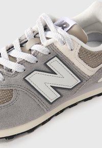 Baskets en daim gris et beige avec des lacets blancs, grand logo "N" cousu sur le côté et semelle en caoutchouc texturée.