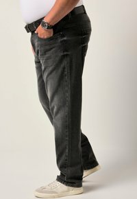 Vaqueros de mezclilla negros con corte recto, llevados a la cintura, que cuentan con bolsillos laterales y zapatillas blancas casuales. Tejido texturizado, sin patrones.