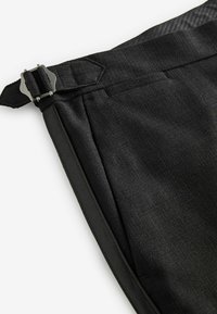Pantalones negros con una tela texturizada, que presentan un cierre lateral, parte frontal plana y una cinturilla suave. El diseño está confeccionado con líneas limpias.