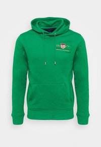 Vihreä puuvillainen huppari, jossa etutasku, säädettävä huppu ja kirjailtu logo, jossa on punaisia ja keltaisia yksityiskohtia. Pehmeä tekstuuri, rento muotoilu.