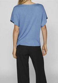 Haut bleu à manches courtes avec une coupe décontractée et un décolleté large, associé à un pantalon noir à jambes larges. Texture lisse et tissu léger.