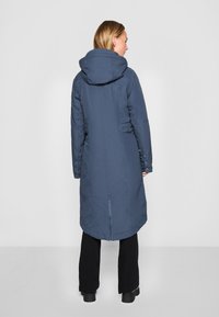 Lange, marineblauwe gewatteerde jas met een capuchon. Voorzien van zijknopen en een rugsplit voor meer bewegingsvrijheid. Glad, waterafstotend materiaal.