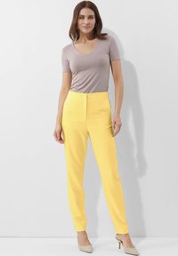 Geel op maat gemaakte broeken met een hoge taille en slim fit, gedragen met een lichtgrijze V-hals top met korte mouwen en beige hoge hakken.