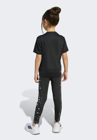 Black athletic t-shirt with short sleeves paired with black leggings featuring a dotted pattern along the sides, worn with white sneakers.
