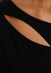Musta paita, jossa on leveä avokaarroke ja leikkauskuvioita. Valmistettu sileästä kankaasta, se on istuva ja siinä on näkyvät saumat.