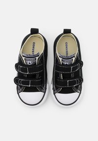 Scarpe da ginnastica nere con punta e suola in gomma bianca. Presentano due strap in Velcro, cuciture bianche a contrasto e un'etichetta "Converse All Star".