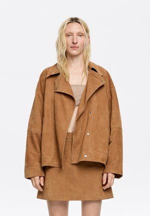 Brown suede oversized jacket with a wide collar and button closure, paired with a matching suede mini skirt. Smooth texture, minimal design.