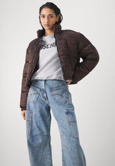Brūns pūkains mētelis ar melnu "Moschino" logotipa apdruku visā virsmā, kombinēts ar pelēku t-kreklu un gaismas zilo brīvi pieguļošu džinsus ar kabatām.