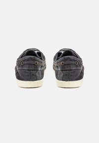 Sivé plátkové slip-on topánky majú textúrovaný zvršok, bielo gumovú podrážku a mosadzné očká na šnúrky. Na zadnej strane sú viditeľné detaily švov.