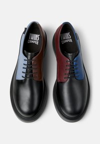 Paire de chaussures en cuir noires à lacets avec des panneaux contrastants bleus et marron, étiquetées "TWINS CAMPER" à l'intérieur.