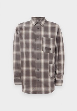 Camisa de cuadro marrón y beige de manga larga con dos bolsillos frontales y collar puntiagudo.