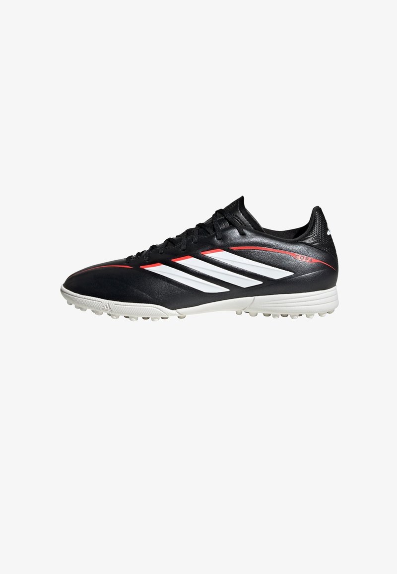 Chaussure de football Adidas noire avec rayures blanches, accents rouges et semelle blanche équipée de petits crampons en caoutchouc pour jeu sur gazon synthétique.