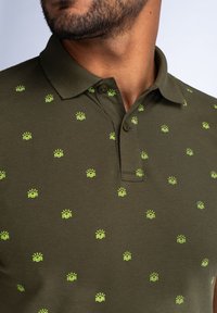 Polo shirt verde oliva realizzato in tessuto intrecciato, con piccoli motivi di sole giallo e onde, dotato di colletto classico e due bottoni.