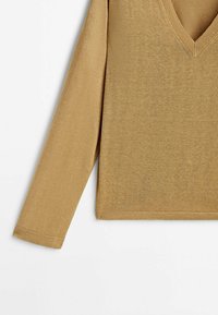 Pull en maille beige à manches longues avec col en V et poignets et ourlet côtelés, posé à plat sur un fond blanc.