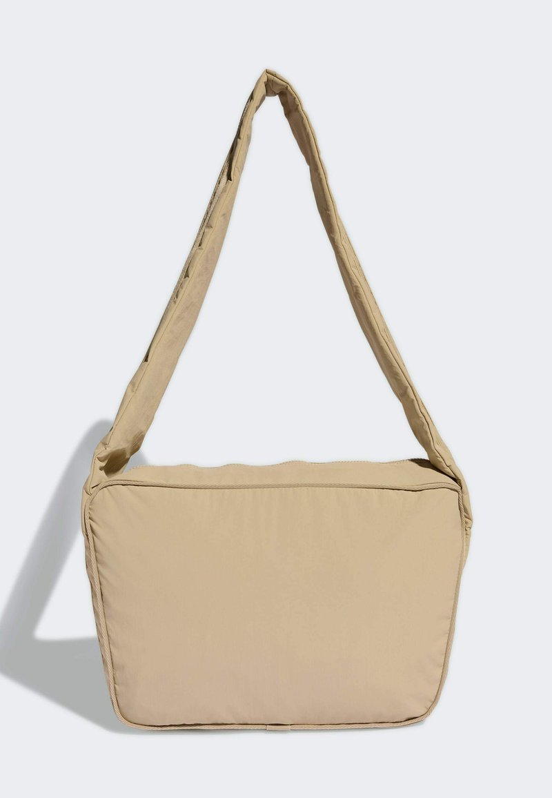 Beige Schultertasche mit einem sanften, gepolsterten Design, ausgestattet mit einem breiten, verstellbaren Trageriemen und einer rechteckigen Form mit abgerundeten Kanten.