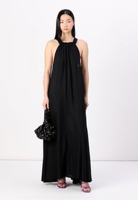 Crna halter maxi haljina s labavim krojem, nabranim dekolteom i lepršavim rubom. Uparen s crnom cvjetnom torbom i ljubičastim sandalama.