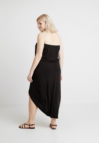 Svart strapless maxiklänning med avslappnad passform, med asymmetrisk fåll och slät textur, i kombination med platta bruna sandaler.