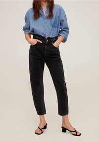 Chemise en denim bleu clair, avec des boutons et des manches retroussées. Jean noir taille haute avec une jambe effilée. Sandales à talons strappés noires.