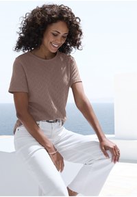 Braun strukturiertes T-Shirt mit Rundhalsausschnitt und kurzen Ärmeln, kombiniert mit weißen Jeans. Lässige Passform, dezentes geometrisches Muster.