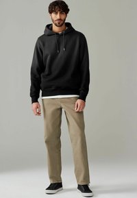 Black sweatshirt with a hood and drawstrings, paired with light brown trousers and black shoes. Smooth texture, casual design.