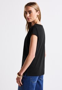 T-shirt noir à manches courtes avec une coupe décontractée, col rond et fentes sur les côtés, associé à un jean en denim bleu. Texture de tissu lisse.
