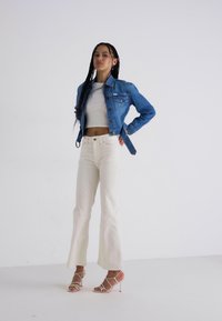 Plava traper jakna, bijeli crop top, kremaste široke hlače i sandale s prozirnim potpeticama. Glatka tkanina, prilagođen silueta i ležeran dizajn.
