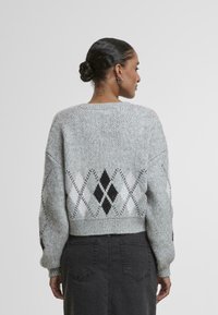 Sivi pleteni pulover s skrajšanim krojem, ki vključuje geometrijski argyle vzorec v črni in beli barvi ter rebraste manšete in rob.
