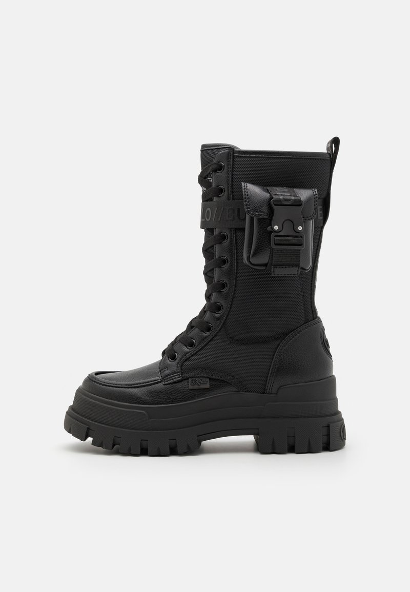 Bottine de combat noire à lacets fabriquée en matériau synthétique. Elle présente un dessus texturé, une semelle épaisse et une accentuation par boucle latérale pour une fermeture sécurisée.