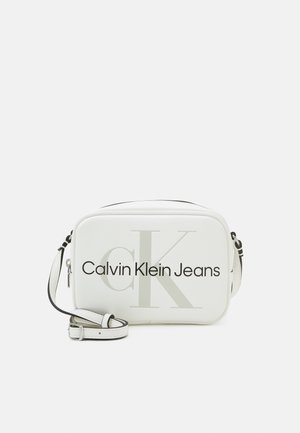 Sac bandoulière rectangulaire blanc avec sangle réglable et logo Calvin Klein Jeans noir ainsi qu'un grand "cK" gris clair à l'avant.