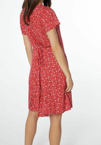 Robe florale rouge à manches courtes, taille cintrée et détail volanté à l'arrière. Le tissu semble léger avec une texture lisse.