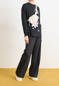 Svart långärmad skjorta med färggårdigt blommönster, matchad med lösa svarta byxor och en ljusfärgad midjeväska. Vita sneakers.