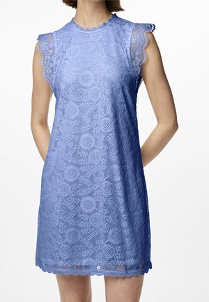 Sleeveless lavender lace dress with floral pattern, scalloped edges on sleeves, neckline, and hem, worn by a person with hands behind back.