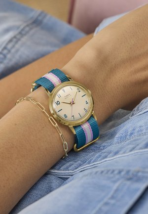 Horloge met gouden kast en een stoffen band met blauwe, roze en witte strepen om de pols, vergezeld van een delicate gouden kettinkarmband.