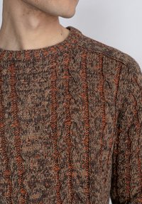 Brown knitted sweater with orange accents, featuring a textured cable pattern. Rounded neckline, long sleeves, and soft fabric texture.