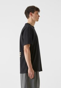 Melna kokvilnas T-krekls ar īsām piedurknēm, apaļš kakla izgriezums, ar zelta tekstu sānos. Taisnas griezuma ar brīvu piegriezumu.