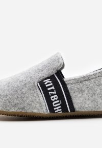 Pantofole grigie in feltro con un elastico nero che presenta il testo bianco "Kitzbühel", suola piatta, forma arrotondata e superficie texture.