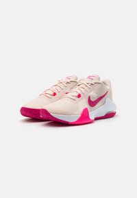 Lichtroze sportschoenen met een gestructureerde bovenkant, contrasterende felroze accenten, witte zolen en een opvallend logo aan de zijkant.