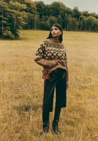 Megzta megztinio šiltų žemės spalvų raštuotas geometrinis raštas, aukšta apykakle ir pūstomis rankogaliais. Derinamas su juodomis kelnėmis ir maža ruda rankine.