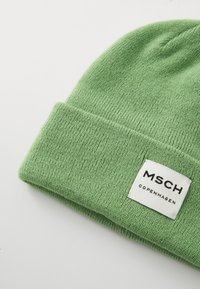 Zielona dzianinowa czapka z wywijanym mankietem, wykonana z miękkiego materiału, z prostokątną białą metką z napisem "MSCH COPENHAGEN."