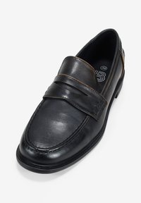 Mocassini in pelle nera con una larga fascetta sul collo del piede, caratterizzati da un design testurizzato e da un sottile punto di cucitura marrone.