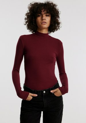 Bordaux ribged lange mouwen body met een hoge nek, gecombineerd met zwarte hooggesneden jeans, met een platte voorkant en vijf knopen als sluiting.