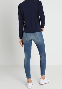 Felpa blu marina con orlo a costine, abbinata a jeans skinny azzurri chiari con finitura sbiadita e dettagli di cucitura laterale, indossati con sneakers bianche.