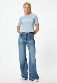 T-shirt a maniche corte cropped di colore blu chiaro, abbinato a jeans in denim a vita alta e gamba larga di lavaggio chiaro. Texture liscia con vestibilità classica.